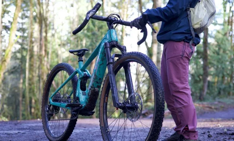 Person with teal mountain bike on a dirt trail in a forest setting.