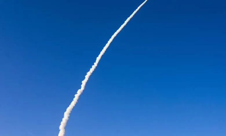 Rocket soars through blue sky, leaving a white smoke trail behind.