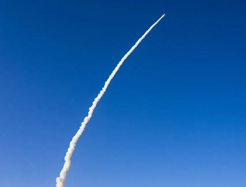 Rocket soars through blue sky, leaving a white smoke trail behind.