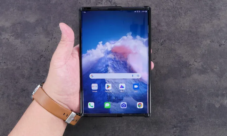 Hand holding a rollable smartphone with a mountain wallpaper.