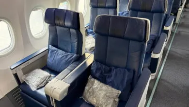 Airplane business class seats with blue leather, pillows, and wrapped blankets.