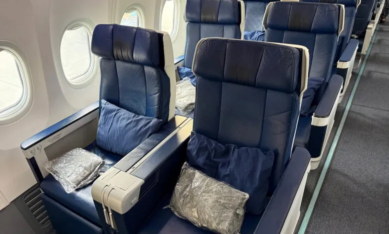 Airplane business class seats with blue leather, pillows, and wrapped blankets.