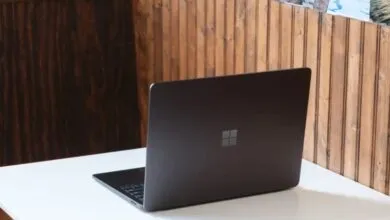 Dark grey Microsoft Surface Laptop on white desk with wood panel background.