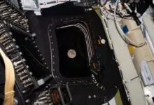 View of the moon through a spacecraft window, surrounded by equipment and wiring.