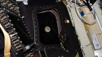 View of the moon through a spacecraft window, surrounded by equipment and wiring.