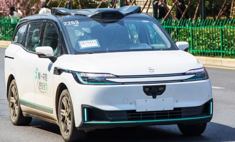 White autonomous vehicle with sensor array on roof driving on city street.