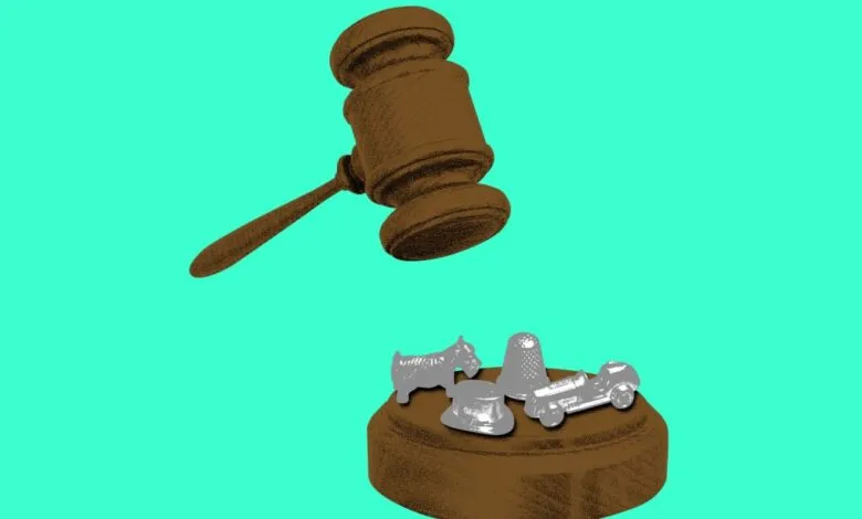 Gavel poised above Monopoly game pieces on a wooden block.