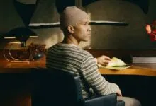 Person with beanie sitting at desk with papers and flowers.