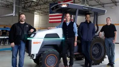 Four men pose with a Monarch electric tractor in a warehouse setting.