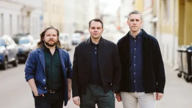 Three men stand side-by-side on a city street, looking directly at the camera.