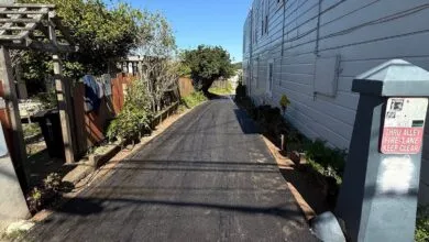 Narrow alleyway between buildings with fresh asphalt and a shadow.