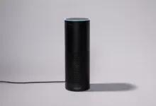 Black Amazon Echo smart speaker with blue light ring on gray background.