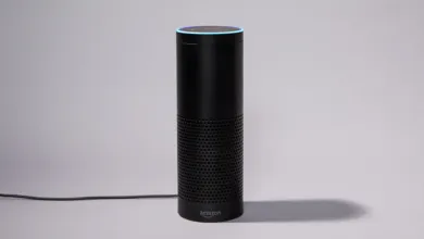 Black Amazon Echo smart speaker with blue light ring on gray background.
