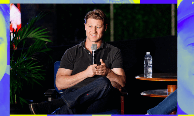 Sean Astin sits on stage, holding a microphone, during a speaking engagement.