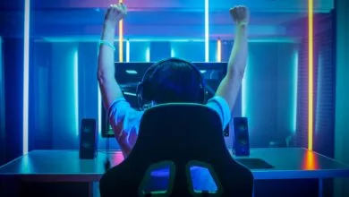 Gamer celebrates victory with arms raised in neon-lit room.