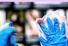 Blue-gloved hand wipes surface with cloth, spray bottle nearby.