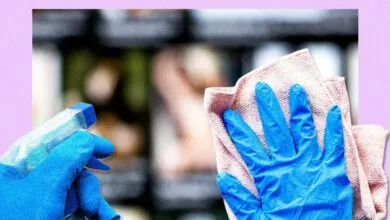 Blue-gloved hand wipes surface with cloth, spray bottle nearby.