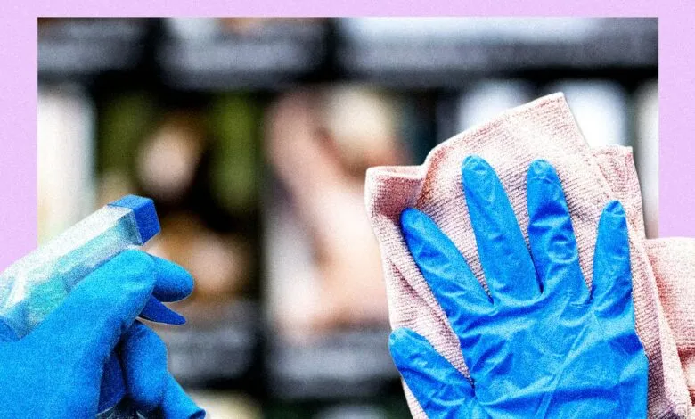 Blue-gloved hand wipes surface with cloth, spray bottle nearby.