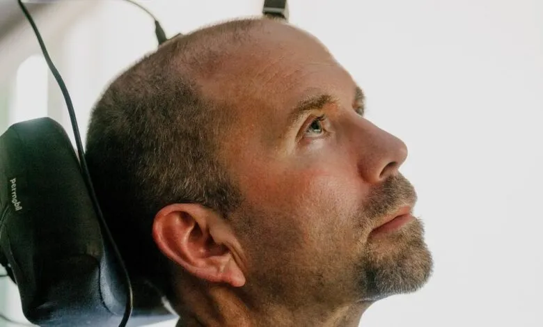 Man in wheelchair with assistive head-mounted technology looks upward.