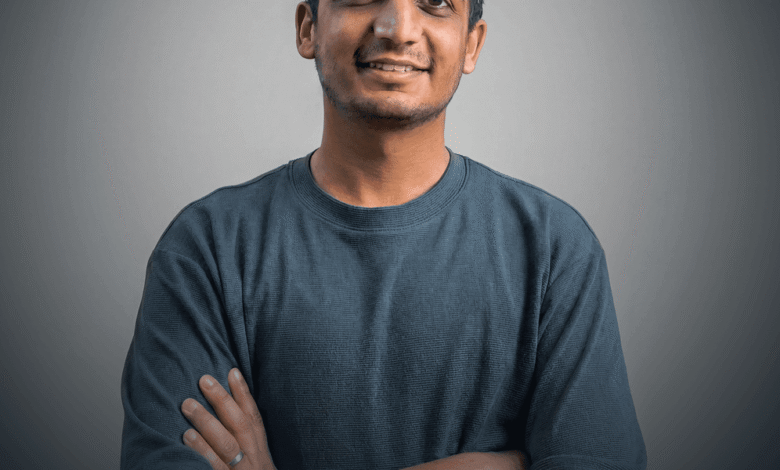 Young Indian man smiles with arms crossed against gray backdrop.