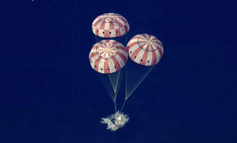 Capsule descends with three red and white striped parachutes against a blue sky.