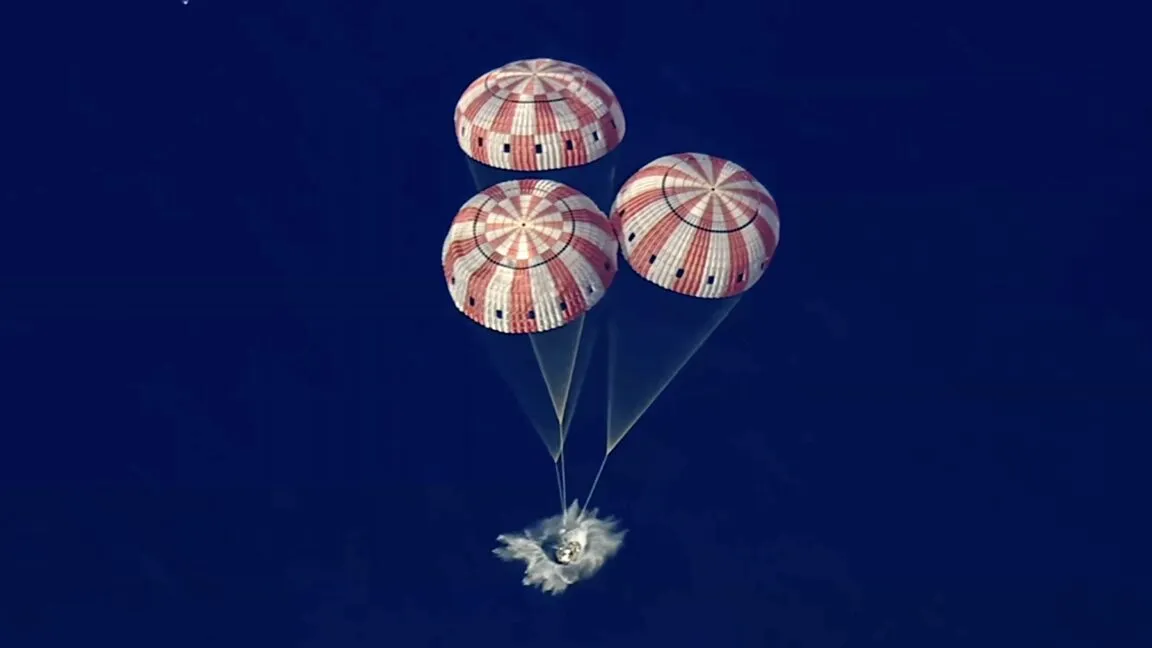 Capsule descends with three red and white striped parachutes against a blue sky.