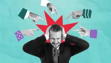 Stressed man surrounded by pointing fingers, feeling blamed.