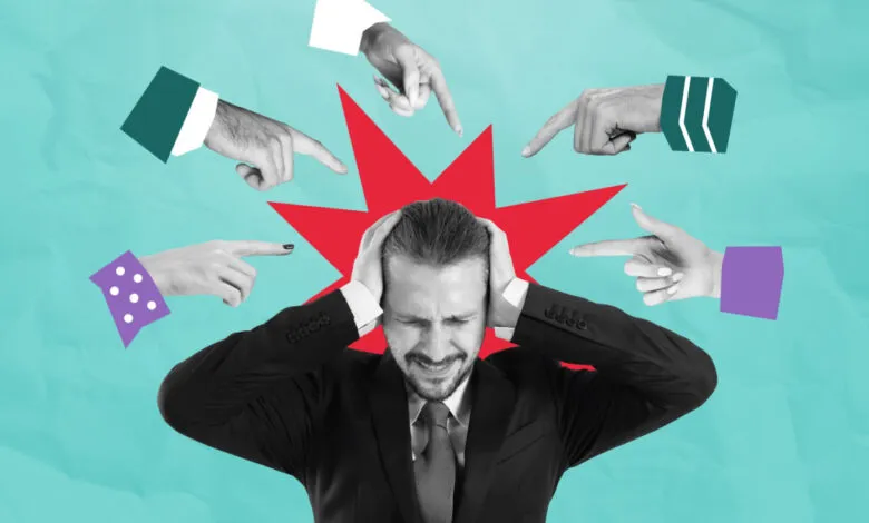 Stressed man surrounded by pointing fingers, feeling blamed.