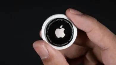 Hand holding an Apple AirTag against a dark background, showing the Apple logo.