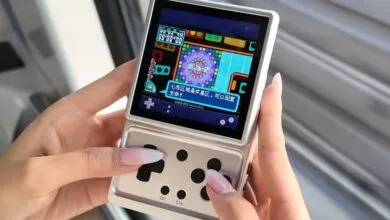 Hands holding silver handheld gaming device with game displayed.