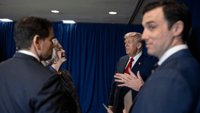Donald Trump speaks to laughing woman surrounded by men in suits.