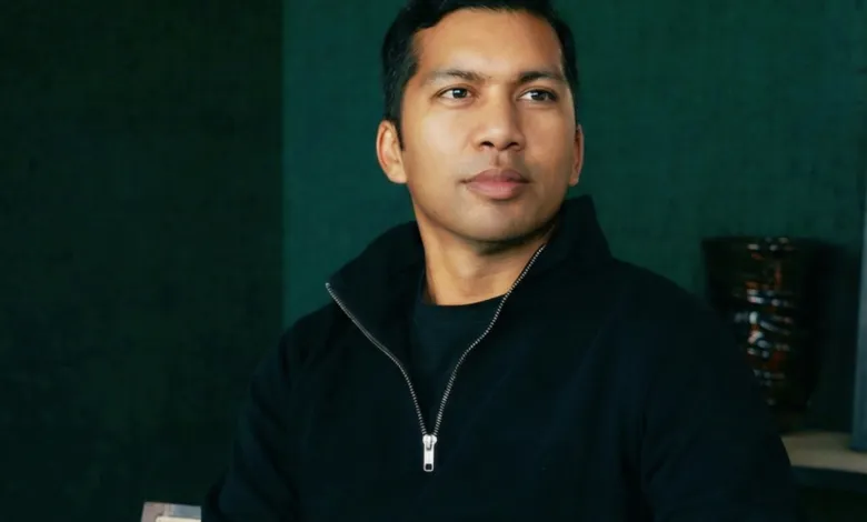 Portrait of a man with dark hair wearing a black zip-up sweater, looking off to the side.
