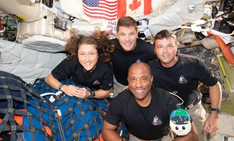Four astronauts smiling in space station, with US and Canadian flags.