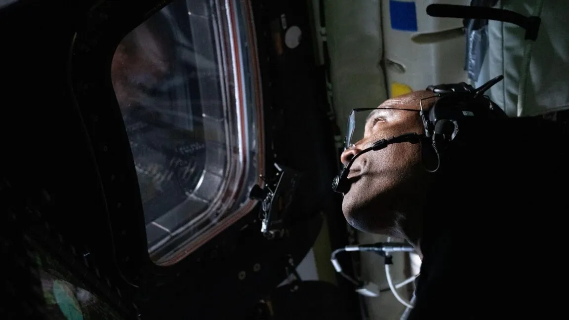 Victor Glover looks out spacecraft window, wearing headset.