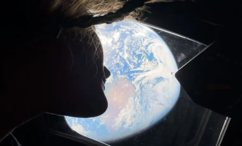 Silhouette of person looking at Earth through a spacecraft window.