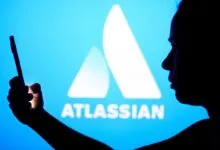 Person silhouetted against Atlassian logo, holding phone.