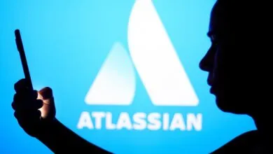 Person silhouetted against Atlassian logo, holding phone.