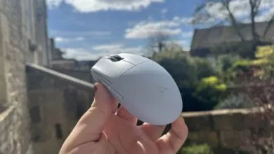 Hand holding a light gray wireless computer mouse outdoors.