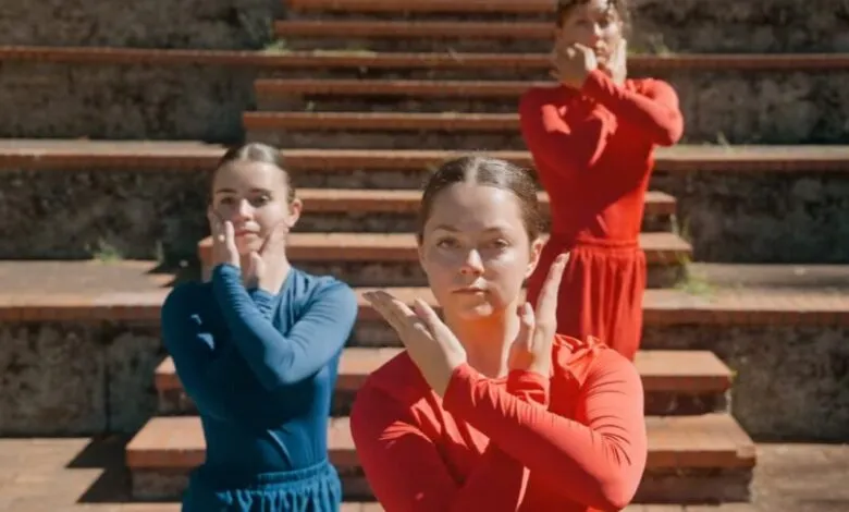 Three dancers in red and blue perform synchronized hand gestures on steps.