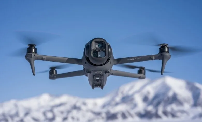 Gray DJI Mavic 4 Pro drone flying against a blue sky and snowy mountains.