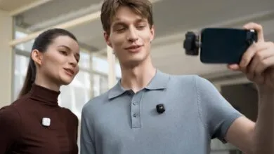 Two people wearing wireless microphones, one taking a selfie with a smartphone.