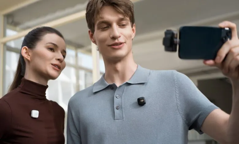 Two people wearing wireless microphones, one taking a selfie with a smartphone.