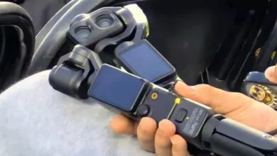 Hand holding a DJI Pocket 3 camera with a wide-angle lens attachment.