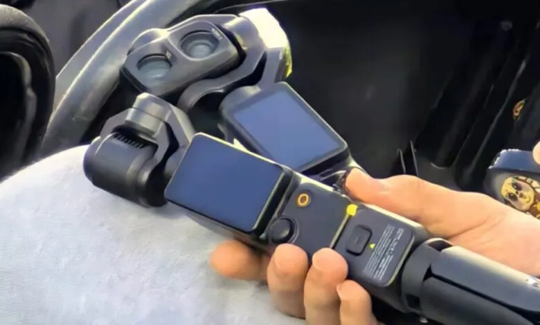 Hand holding a DJI Pocket 3 camera with a wide-angle lens attachment.