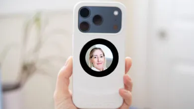 Hand holds phone with woman's face visible in circular window on the back.