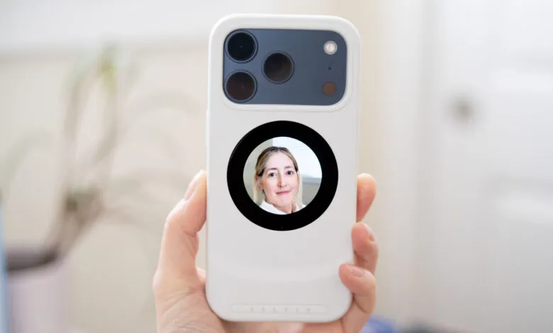 Hand holds phone with woman's face visible in circular window on the back.