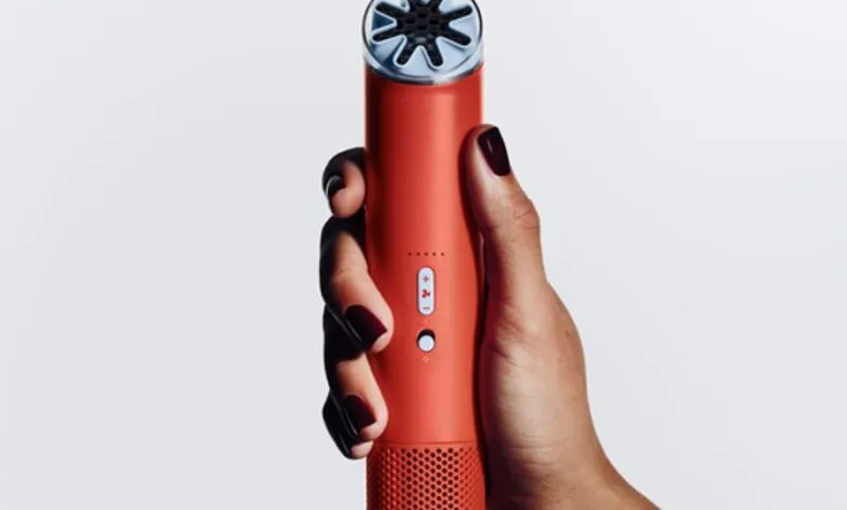 Hand holding a coral-colored portable air purifier against a white background.