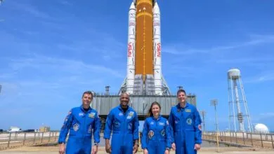 Four astronauts in blue suits stand before the Artemis 1 rocket.