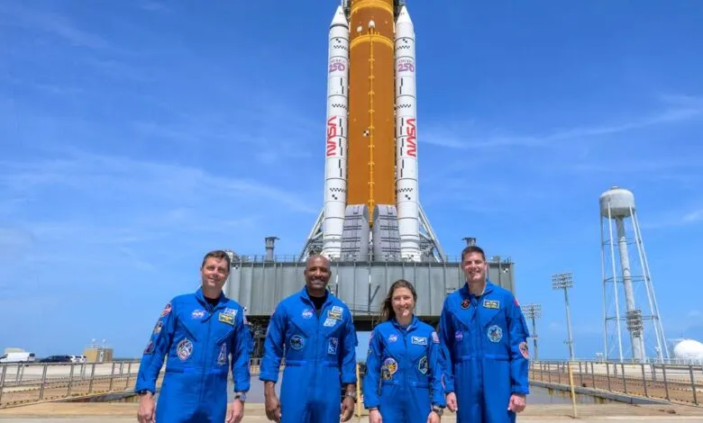 Four astronauts in blue suits stand before the Artemis 1 rocket.