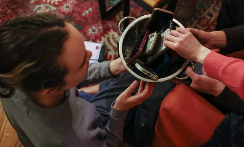 People reaching into colander filled with smartphones.